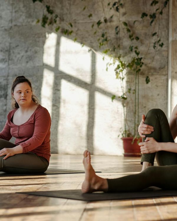 Person stretching gently on a yoga mat in a bright, sunlit room.
